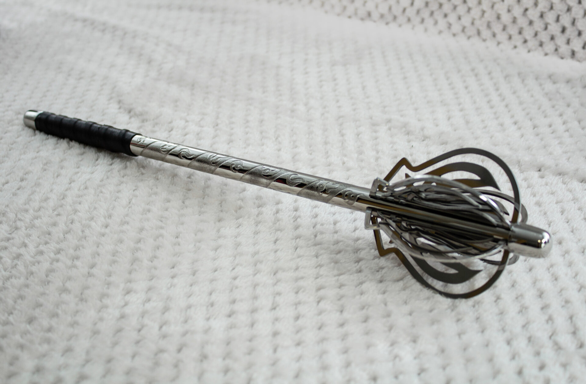 Pernach laid on pale fabric, showing its openwork head, patterned shaft and black wrapped grip