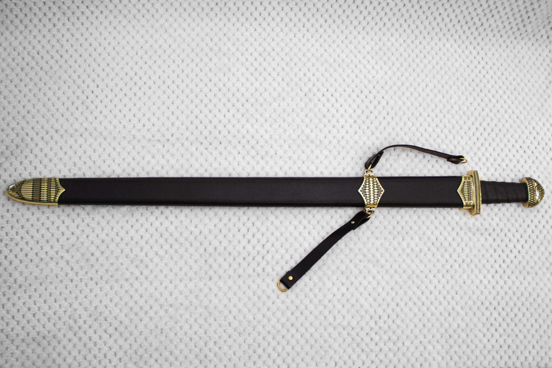 Full side view of Sviatoslav's sword in a black scabbard with patterned fittings and carrying straps