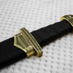 Patterned pommel, guard and scabbard mouth around the black grip of sheathed Sviatoslav's sword