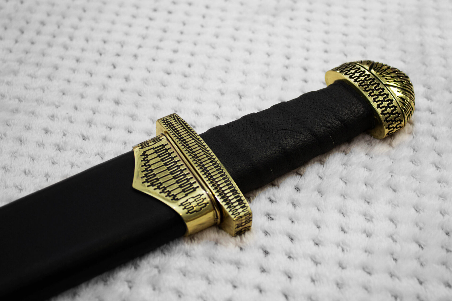 Patterned pommel, guard and scabbard mouth around the black grip of sheathed Sviatoslav's sword