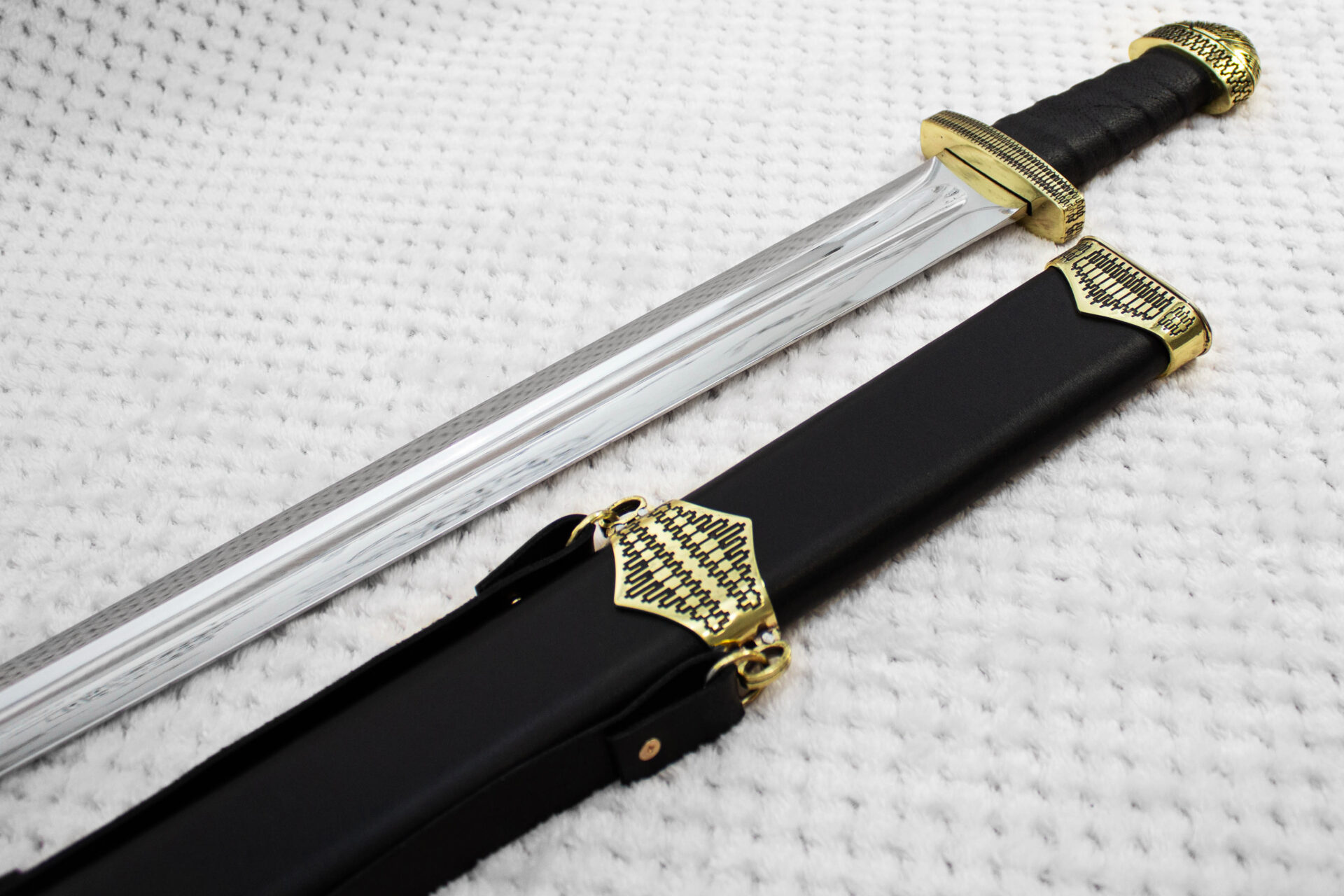 Sviatoslav's sword beside a black scabbard, showing the blade, wrapped grip and patterned fittings
