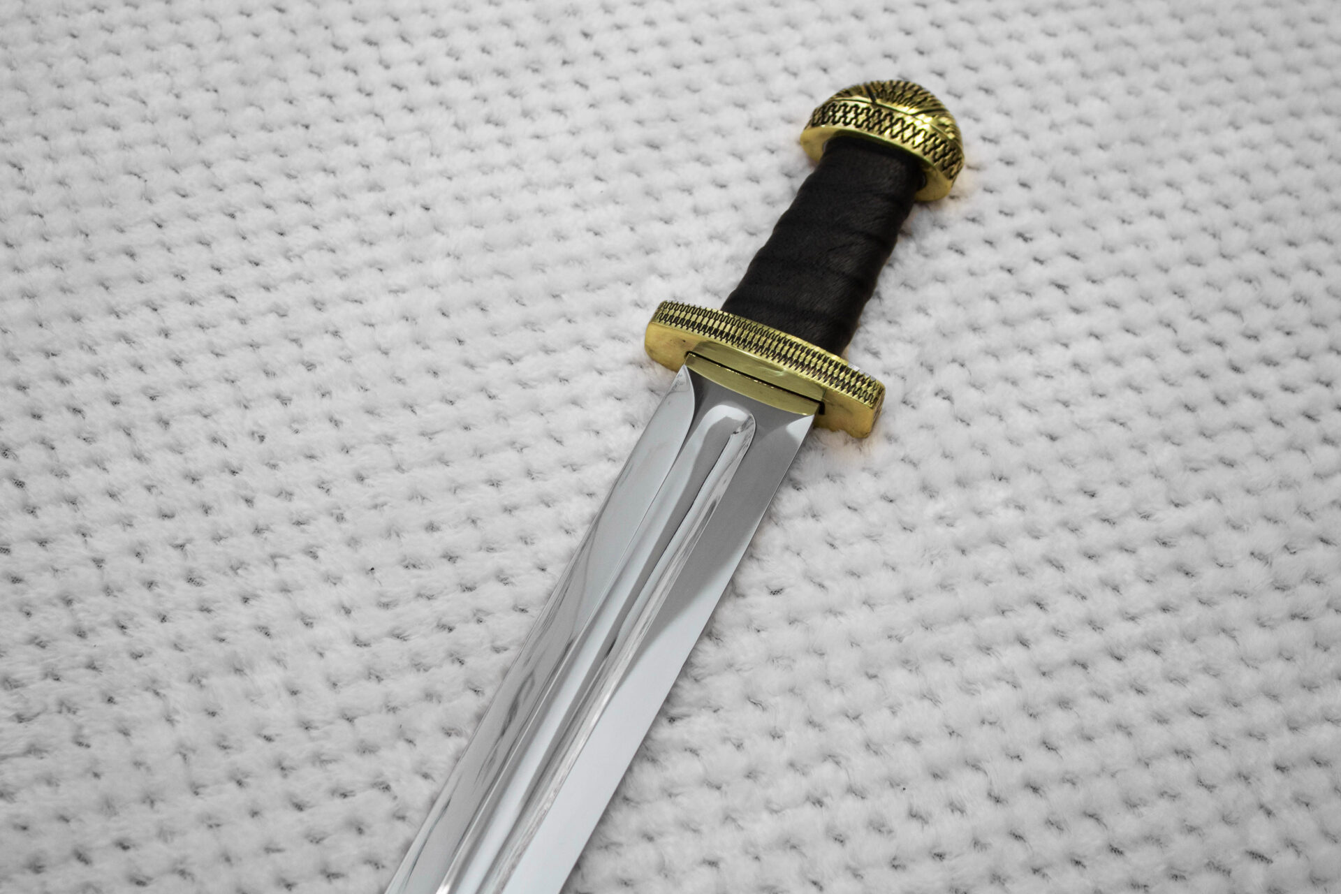 Sviatoslav's sword hilt and blade base, showing a black grip, patterned guard and deep central fuller