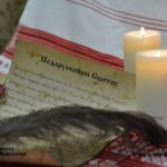 Unrolled gift scroll with Ukrainian text and a wax seal beside lit candles on a red-and-white embroidered cloth