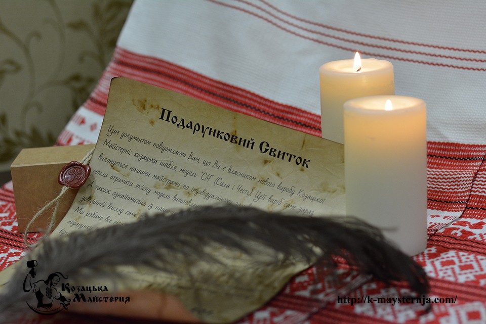 Unrolled gift scroll with Ukrainian text and a wax seal beside lit candles on a red-and-white embroidered cloth