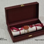 Rolled gift scroll with a wax seal and burgundy ribbons inside an open presentation box