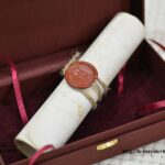 Close-up of a wax seal and twine on a rolled gift scroll inside an open burgundy presentation box