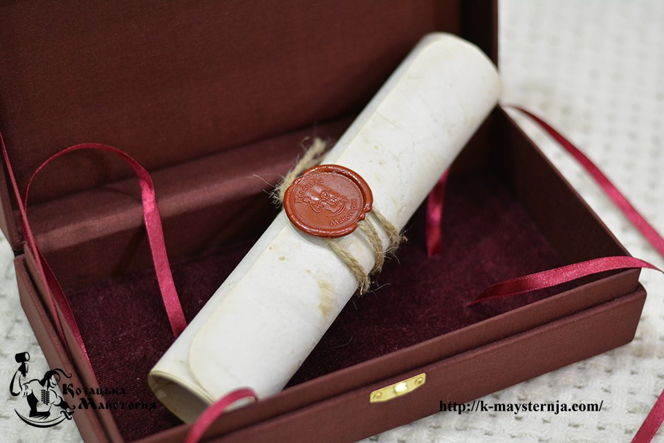 Close-up of a wax seal and twine on a rolled gift scroll inside an open burgundy presentation box