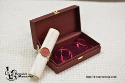 Rolled gift scroll with a wax seal beside an open presentation box lined with red fabric