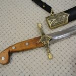 Close-up of the unsheathed SiCh-Sh hilt and blade beside the decorated scabbard throat