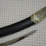 Decorated SiCh-Sh scabbard tip beside the exposed blade tip, close-up at an angle
