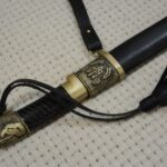 Cossack shashka in a black scabbard: close-up of the trident-decorated fitting, carrying strap and tassel