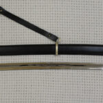 Full-length unsheathed Cossack shashka beside its black scabbard, carrying straps and tassel