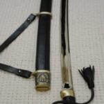 View along the unsheathed Cossack shashka and black scabbard from the decorated hilt toward the tips