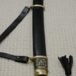 Cossack shashka in a black scabbard, viewed lengthwise from the decorated pommel toward the scabbard tip
