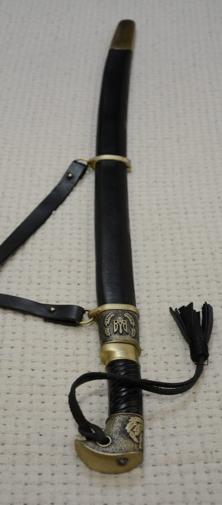 Cossack shashka in a black scabbard, viewed lengthwise from the decorated pommel toward the scabbard tip