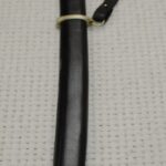 Cossack shashka in its black scabbard with carrying straps, viewed from the scabbard-tip end toward the tasselled hilt