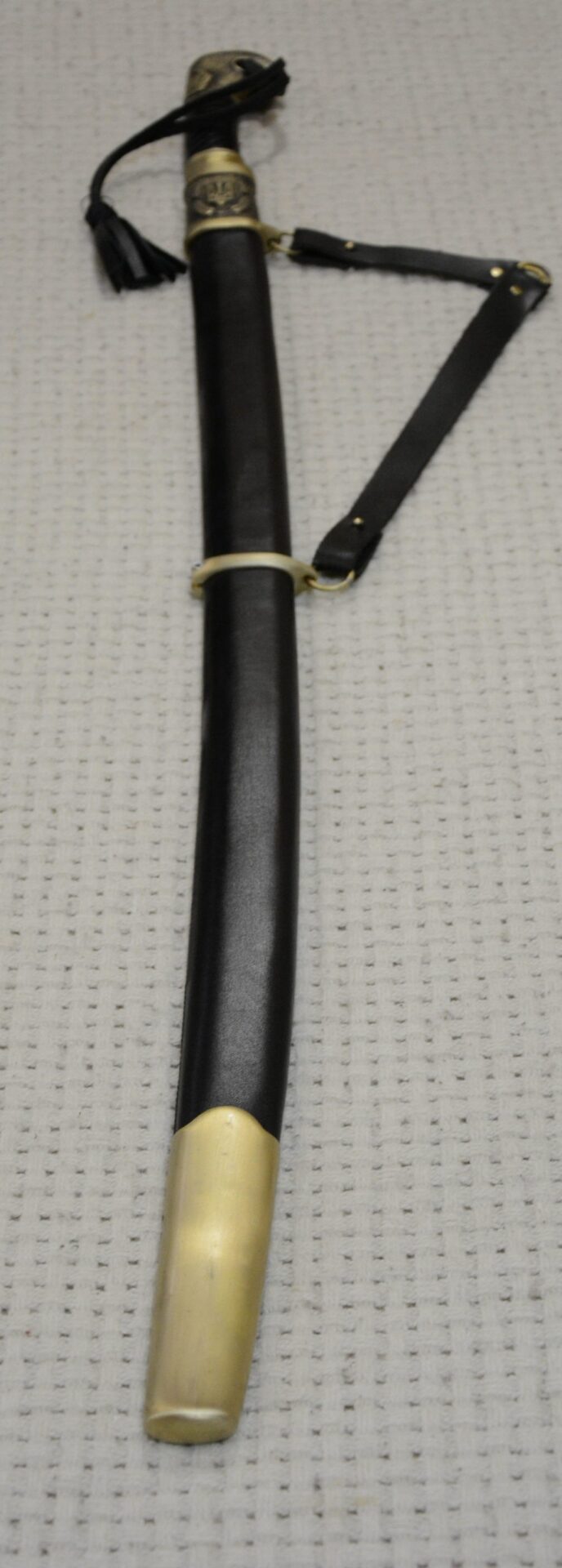 Cossack shashka in its black scabbard with carrying straps, viewed from the scabbard-tip end toward the tasselled hilt