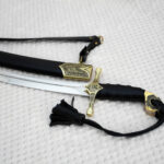 SiCh-Hetman saber hilt and blade beside the patterned mouth of its black scabbard and carrying strap