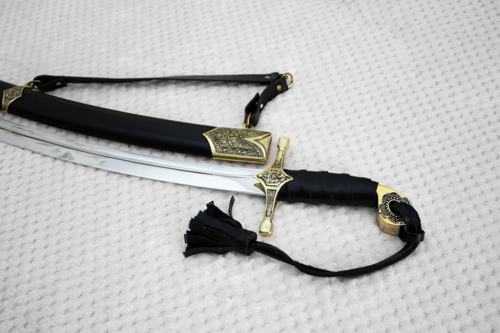 SiCh-Hetman saber hilt and blade beside the patterned mouth of its black scabbard and carrying strap