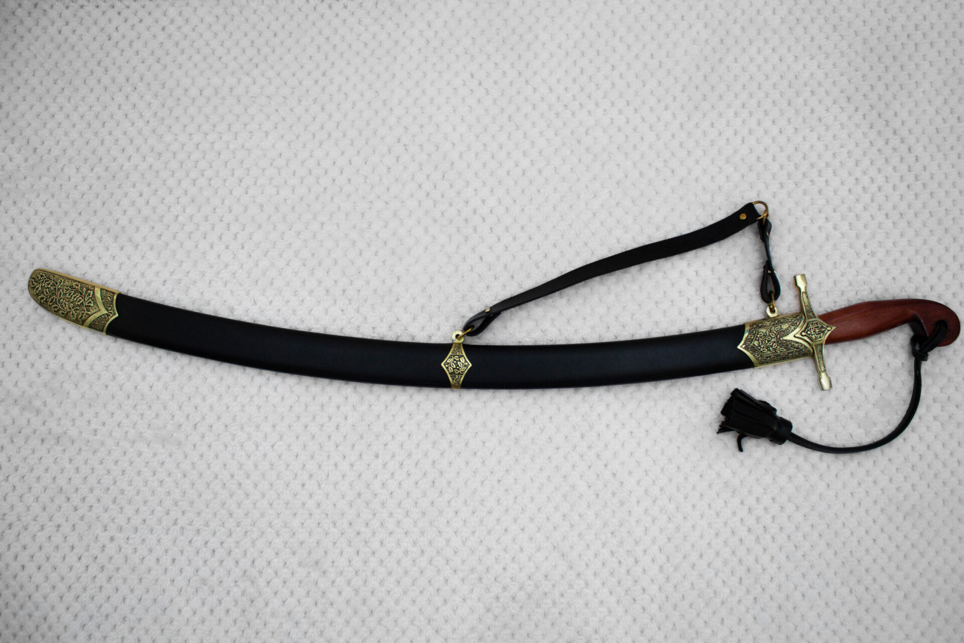 Full side view of the SiCh-Souvenir saber in its black scabbard with patterned fittings and carrying strap