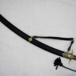 SiCh-Souvenir saber in a curved black scabbard with decorated tip and carrying strap, diagonal view