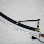 SiCh-Souvenir curved blade beside its black scabbard, with decorated scabbard tip and carrying strap