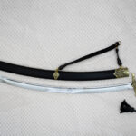 Full side view of the unsheathed SiCh-Souvenir saber below its black scabbard with decorated fittings