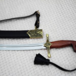 SiCh-Souvenir saber blade and brown hilt below a black scabbard with patterned mouth and carrying strap