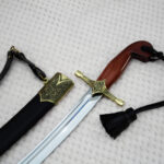 SiCh-Souvenir saber hilt beside its scabbard mouth, showing brown grip, ornamented guard and black straps