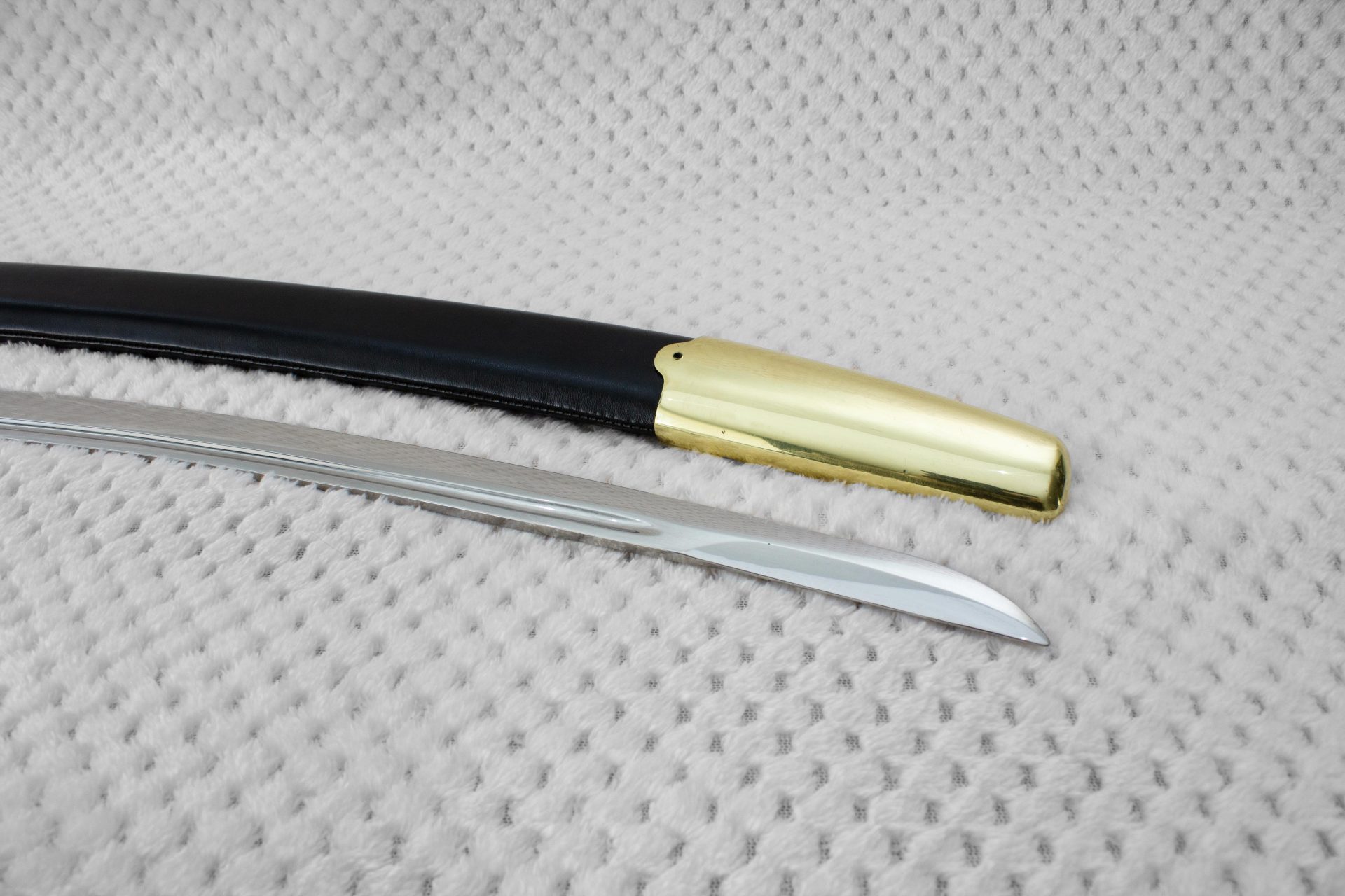 Close-up of the Dragoon saber blade tip beside the smooth metal tip of its black scabbard