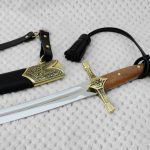 SiCh-K saber beside its black scabbard, showing the brown grip, decorated guard and tassel